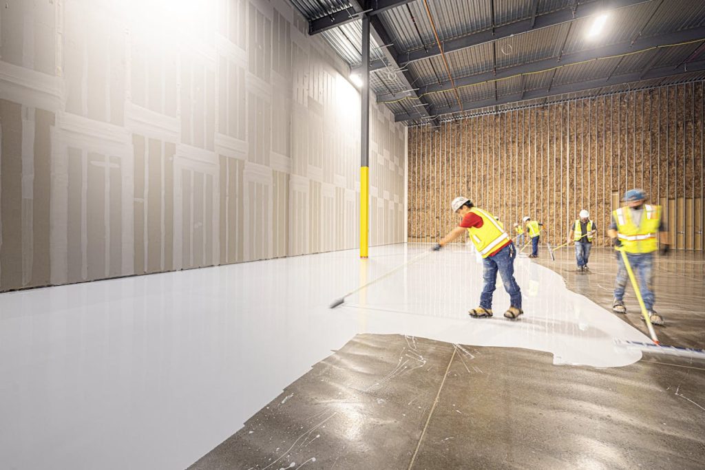 Construction workers in hard hats and vests laying a fresh concrete floor inside a building in Dallas, Texas.