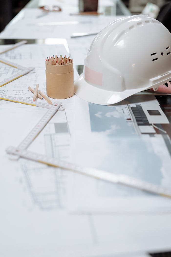 A detailed view of an architect's desk with plans, a hard hat, and drafting tools.